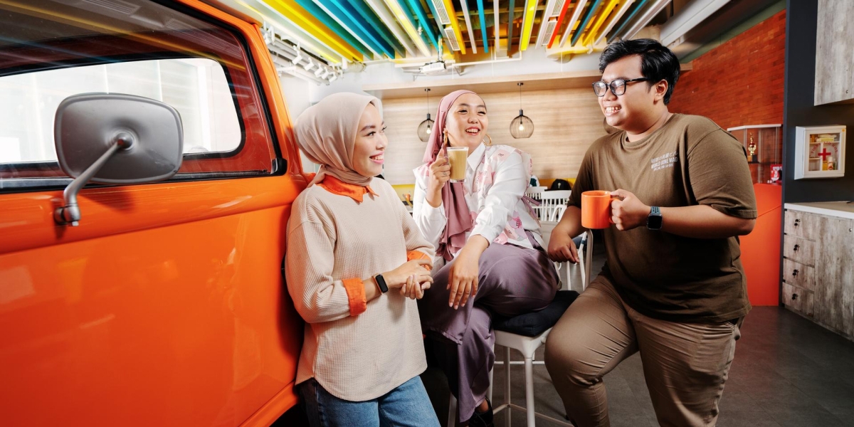 Dua perempuan berhijab dan seorang laki laki berkacamata sedang menghabiskan waktu bersama sambil ngopi di sebuah cafe modern.