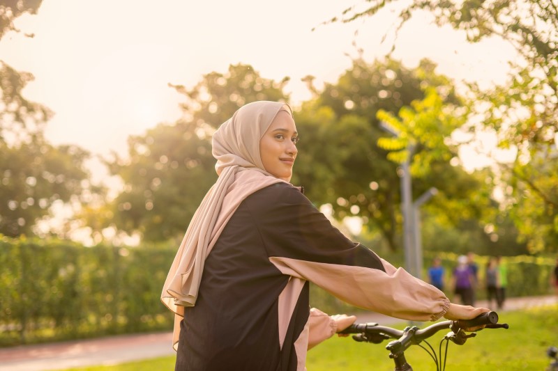 Wanita berhijab mengendarai sepeda di taman saat matahari terbit