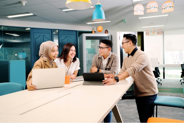 Dua pria dan dua wanita pekerja kantor sedang berdiskusi bersama di ruang rapat terbuka sebuah kantor.