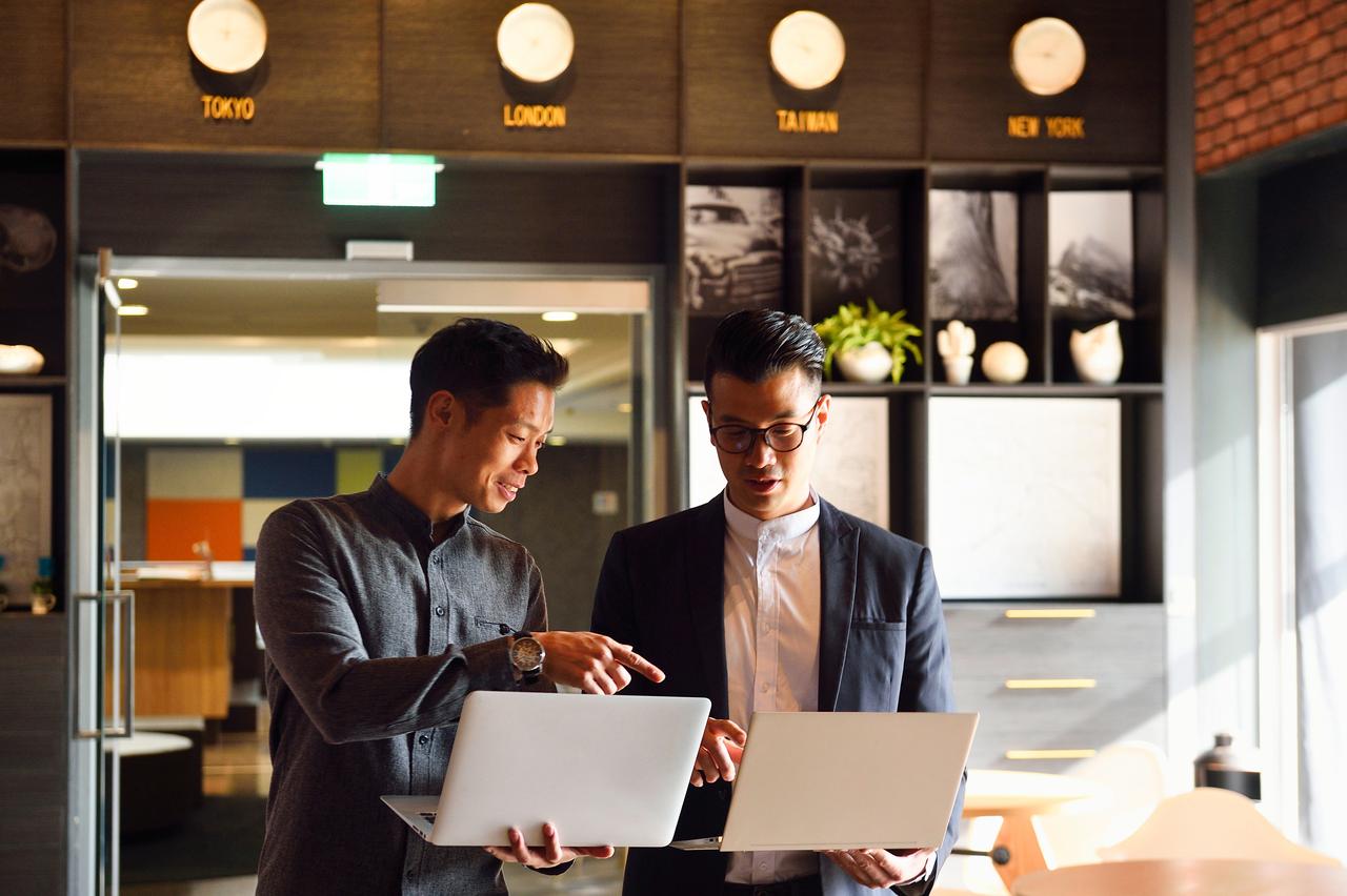 Men_standing_with_laptops_in_an_office.jpg